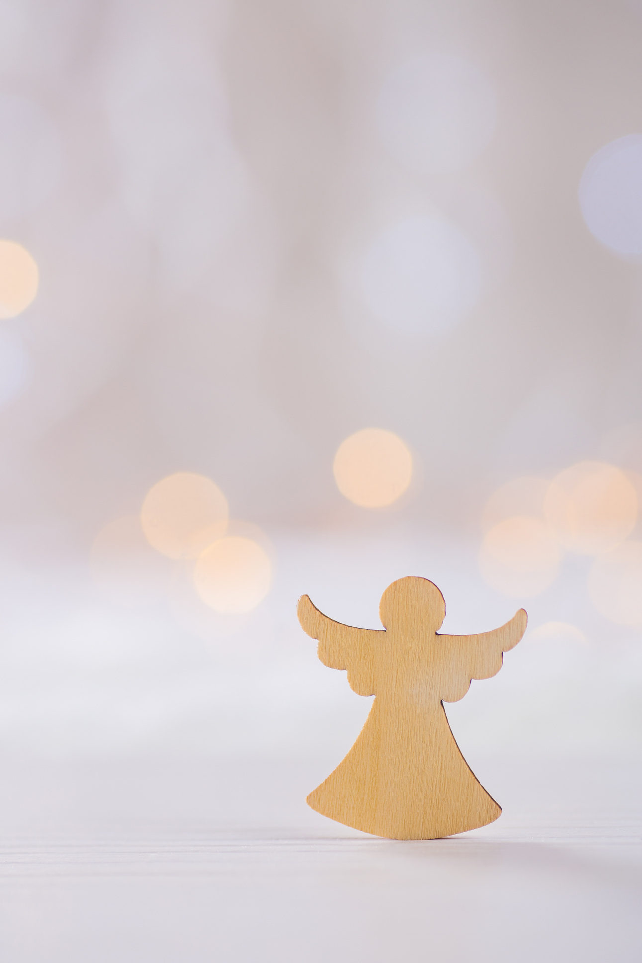 Wooden icon of Christmas angel on light bokeh background